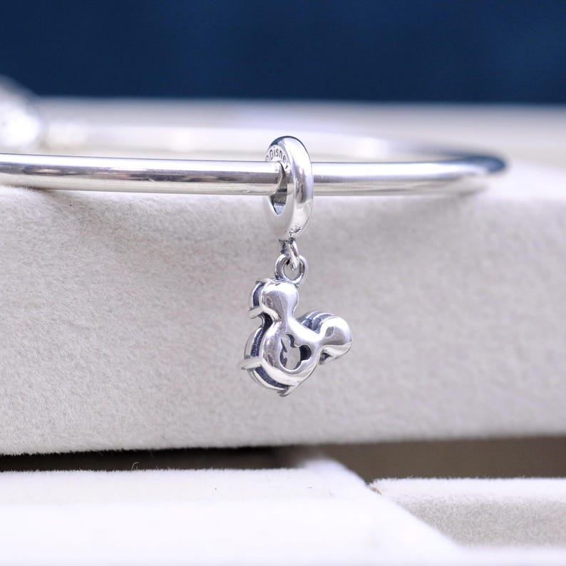May include: Silver charm in the shape of Mickey Mouse, hanging from a silver bracelet.