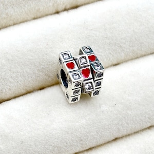 May include: Silver charm with a red heart design and clear cubic zirconia stones. The charm is in the shape of a cube and has a layered design.