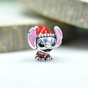 Puede incluir: Un abalorio de plata con la forma del personaje Stitch, que lleva un gorro de Pap&aacute; Noel rojo y un abrigo rojo a juego. El personaje tiene grandes orejas con el interior rosa, ojos negros y una nariz peque&ntilde;a, con detalles en esmalte rojo.
