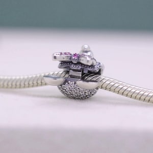 May include: A silver charm with a butterfly design, featuring pink and clear gemstones. The charm is attached to a silver snake chain bracelet. The butterfly has pink gemstones on the wings and clear gemstones on the body.