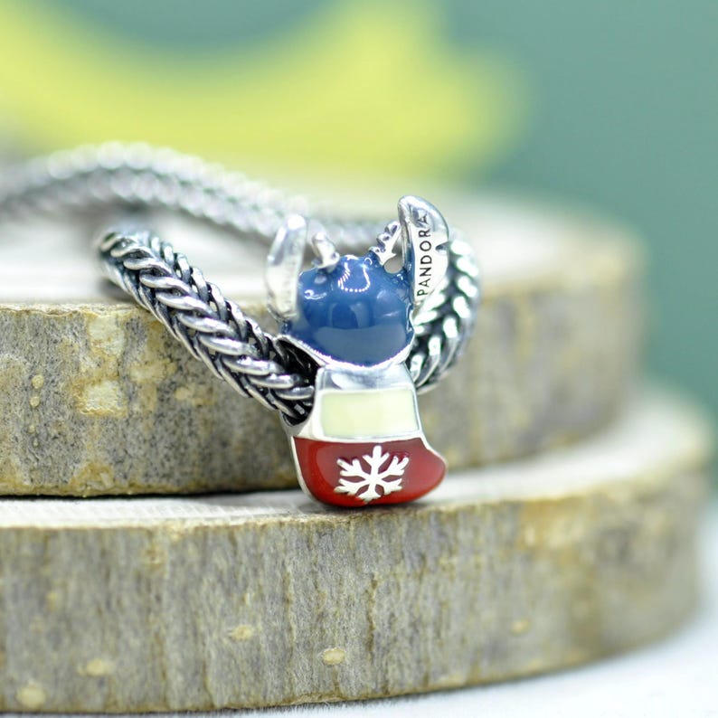 Puede incluir: Un charm de plata con forma de calcet&iacute;n esmaltado en azul, blanco y rojo con un detalle de copo de nieve blanco. El charm est&aacute; ensartado en una cadena de plata trenzada y la palabra PANDORA est&aacute; grabada en el lateral de la parte superior.