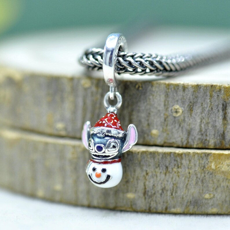 Puede incluir: Un dije de plata que muestra un personaje azul con orejas grandes que lleva un gorro de Pap&aacute; Noel rojo y blanco, colocado sobre una cabeza de mu&ntilde;eco de nieve blanca con una nariz naranja peque&ntilde;a y una sonrisa negra, colgado de una cadena.