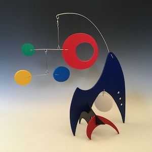 May include: A colorful mobile sculpture with geometric shapes in red, blue, yellow, and green. The mobile is suspended from a metal rod and features a blue, white, and red abstract form at the base.