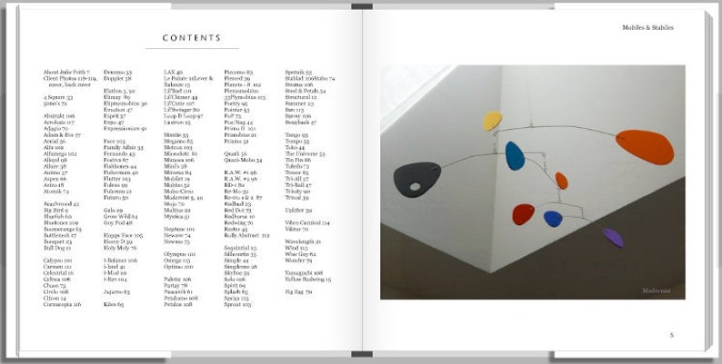 May include: A mobile sculpture with colorful, abstract shapes hanging from thin wires. The shapes are in shades of red, orange, yellow, blue, and purple. The mobile is suspended from the ceiling of a white room.