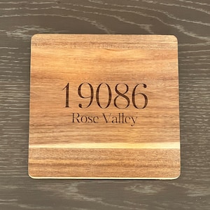 May include: A square wooden coaster featuring a natural light and dark brown wood grain pattern. The center of the coaster is engraved with the number 19086 in a bold serif font, followed by the text Rose Valley in a smaller serif font below it.