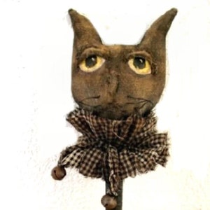 May include: A brown fabric cat head with yellow eyes and a brown and white checkered fabric collar with bells attached to the bottom. The cat head is attached to a metal rod.