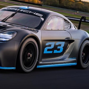 May include: A black and blue Porsche race car with the number 23 on the side, driving on a race track.
