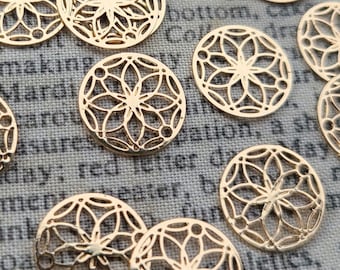 May include: A collection of gold-colored metal charms featuring a delicate, intricate mandala design. The charms are circular and have a cutout pattern.