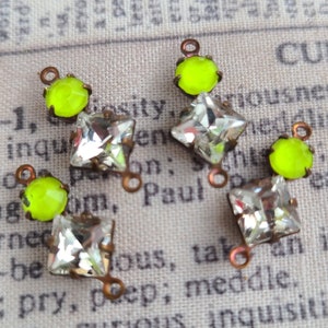 May include: Four decorative jewelry components. Each piece features a clear, square-cut crystal below a neon green, round stone. The crystals are set in a copper-colored metal with a small loop at the bottom for attachment. These components are ideal for jewelry making.