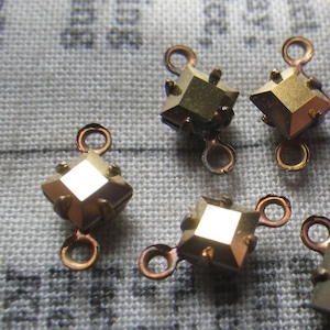 May include: Six gold-toned metal square-shaped charms with a clear rhinestone in the center. Each charm has two loops on the side for attaching to jewelry or other crafts.