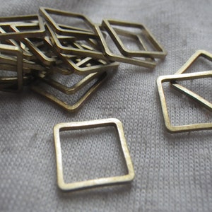 Könnte beinhalten: Ein Stapel goldfarbener quadratischer Sprungringe aus Metall. Die Ringe sind übereinander gestapelt und einige liegen flach auf einer weißen Stoffoberfläche.