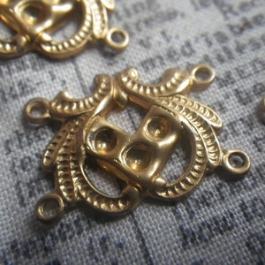 May include: Close-up of several gold-colored filigree connectors. Each connector features an ornate design with loops and decorative elements, and small holes for attaching to other components. The connectors are likely for jewelry making or crafting.