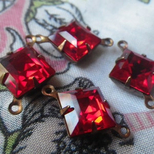 May include: Four square, faceted, red glass jewels with brass findings. Each jewel has a brass loop for attaching to a project. The jewels are set in brass prongs.