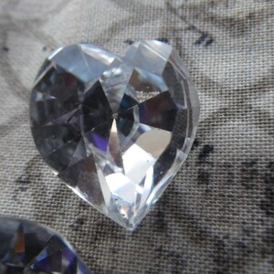 May include: A clear crystal heart-shaped prism with many facets. The prism is reflecting light and creating a rainbow effect.