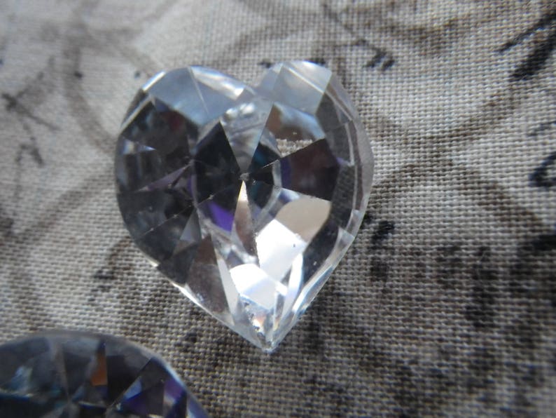 May include: A clear crystal heart-shaped prism with many facets. The prism is reflecting light and creating a rainbow effect.
