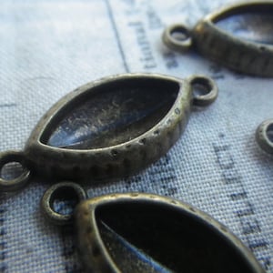 May include: Four antique bronze metal pendant settings with a teardrop shape and a small loop on each side. The settings are designed to hold a cabochon stone.