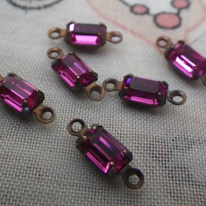 May include: Several small, rectangular, magenta-colored glass rhinestones with bronze-colored metal settings and loops. These vintage-style components are ideal for jewelry making or craft projects.