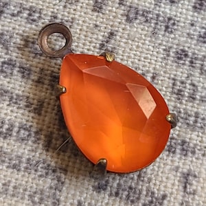 May include: A teardrop-shaped orange glass pendant with a bronze metal setting and a loop for hanging.