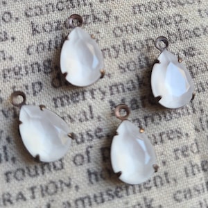 May include: Four pear-shaped, opalescent glass pendants with bronze-colored metal settings and loops. The pendants are arranged on a textured, off-white surface, showcasing their delicate, vintage aesthetic. The glass has a soft, milky appearance.
