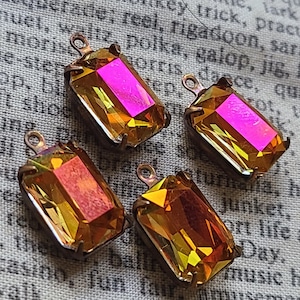 May include: Four rectangular, iridescent crystal pendants with a copper-coloured metal setting. The crystals shift from yellow to orange and pink, with a small loop at the top for attaching to jewellery.