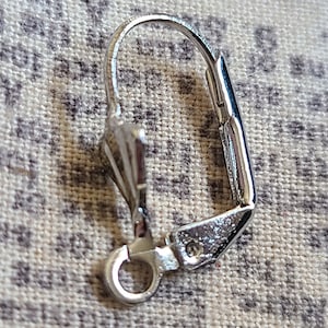 May include: Silver earring hook with a small loop at the bottom and a curved wire that closes with a push-back clasp.