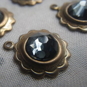 May include: A close-up of a gold-toned metal pendant with a faceted black gemstone in the center. The pendant has a scalloped edge and a loop for attaching a chain.