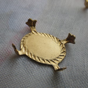 May include: A gold-colored metal decorative stand with a round top and three legs. The stand has a rope-like design around the edge of the top.