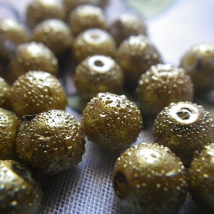 Puede incluir: Primer plano de una colección de cuentas doradas con superficie texturizada. Las cuentas están dispuestas en un patrón aleatorio y todas son del mismo tamaño.