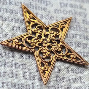 Puede incluir: Una estrella de metal de color dorado con un diseño de filigrana. La estrella es intrincada y detallada, con un delicado patrón de espirales y bucles.