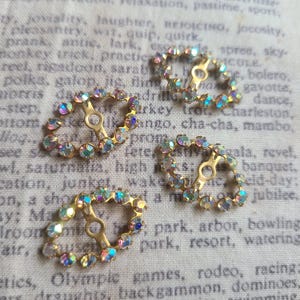 May include: Four vintage gold-toned oval buckles with iridescent rhinestones. Each buckle has a central bar and is surrounded by a row of colorful, sparkling stones. These decorative buckles are ideal for embellishing clothing or accessories.