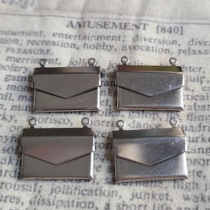 May include: Four silver metal envelope-shaped charms with two jump rings on each. The charms are on a fabric background.