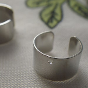 May include: Two silver ear cuffs, one with a small hole in the center. The cuffs are simple and minimalist in design.