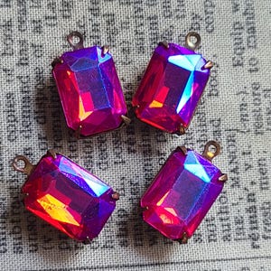Puede incluir: Cuatro colgantes rectangulares de cristal iridiscente con una vibrante mezcla de tonos rosa, morado y azul. Cada colgante tiene un engaste de metal color bronce y un pequeño lazo en la parte superior.