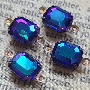 May include: Four rectangular, iridescent blue and purple glass jewels with copper-colored metal loops. The jewels have a faceted cut, reflecting light with a range of colors. These vintage-style components are suitable for jewelry making.