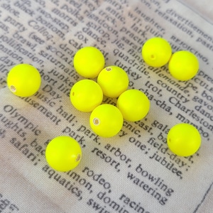 Può includere: Un gruppo di dieci perline rotonde di colore giallo brillante, sparse su una superficie di tessuto con testo stampato.