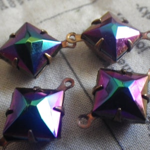 Può includere: Quattro decorazioni metalliche quadrate iridescenti con due anelli su ogni lato. Le decorazioni hanno una finitura arcobaleno con sfumature di viola, blu e verde.