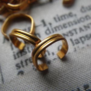 May include: Two gold-toned metal rings with a double-layered design. The rings are interlocked and have a smooth, polished finish.