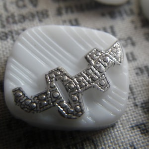 May include: White button with a silver, decorative, swirl design.