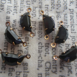 May include: Six black half-circle glass beads with gold metal connectors. The beads are faceted and have a shiny finish.