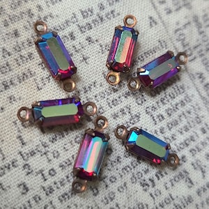 May include: Six iridescent purple and green rectangular glass beads with copper-toned metal connector loops. The beads have a faceted design.