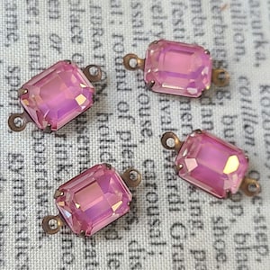 May include: Four pink glass connector charms with a metal loop on each side. The charms are rectangular and have a faceted design.