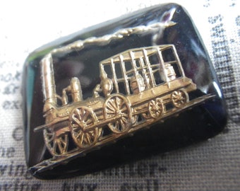 May include: A gold-colored train engine with black wheels and a black background. The train engine has a smoke stack and a caboose.