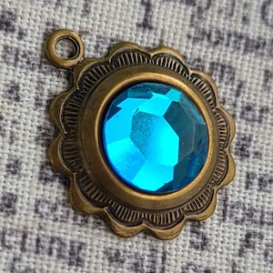 May include: A blue gemstone set in a gold-toned metal pendant with a scalloped edge.
