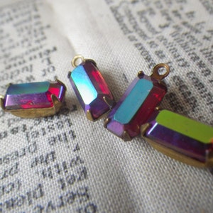 May include: Four iridescent glass charms with gold metal settings. The charms are rectangular and have a variety of colors, including red, blue, green, and purple.
