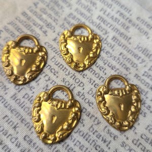 May include: Four gold-toned heart-shaped lock charms with intricate details. Each charm has a keyhole and a loop for attaching to a necklace or bracelet.