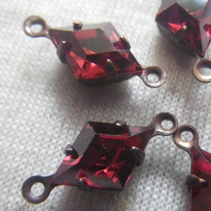 May include: Close-up of several faceted, diamond-shaped, red glass pendants with a metallic loop at the top. The pendants have a dark, antique-style metal setting.
