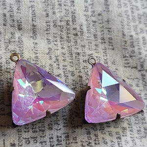 May include: Two iridescent pink triangle-shaped glass charms with a metal loop at the top. The charms have a faceted design and are set on a metal base.
