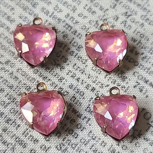 May include: Four pink heart-shaped glass charms with a metallic finish. Each charm has a loop at the top for attaching to a necklace or bracelet.