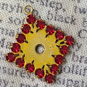 May include: A gold-toned pendant with a round center hole and a border of red rhinestones.