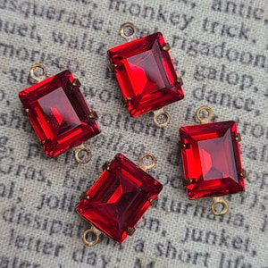 Puede incluir: Cuatro piedras rectangulares de cristal rojo en engastes de latón. Cada piedra presenta una superficie facetada y está sujeta por cuatro pequeñas garras. Cada engaste incluye dos pequeños bucles circulares en los extremos para conectar piezas.